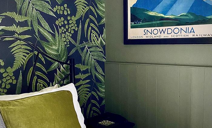 A bedroom at Crafnant House with a green wall, a leaf patterned wallpaper, a green cushion on a white bed and a poster saying "SNOWDONIA"